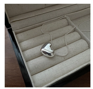 Close-up of a polished heart pendant on a bead chain inside a beige jewelry box