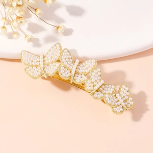 Detail of a golden alloy butterfly hair clip with faux pearls on a beige stand