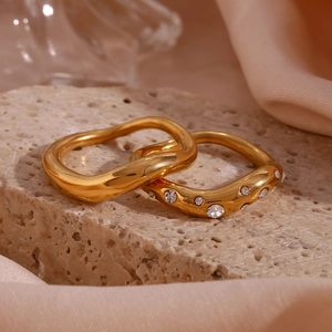 Detail of two 18K gold plated wavy rings with micro-inlays on a stone surface