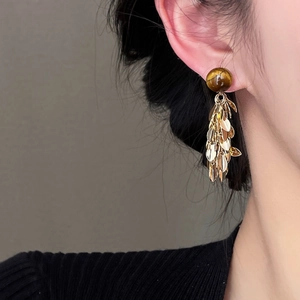 Detail of tiger eye stone bead and golden leaf tassel drop earrings on a model
