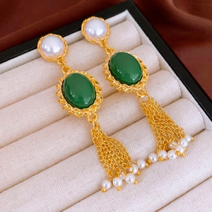 Détail de boucles d'oreilles dorées à pompons avec pierre ovale verte et perles
