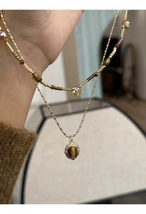 Macro detail of gold-plated beaded necklace featuring an oval tiger eye stone pendant