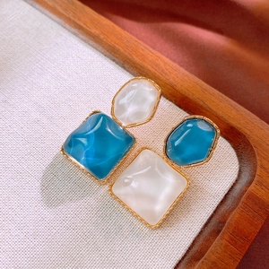 Details von geometrischen Goldohrringen mit blauem und weißem Harz auf Holztablett