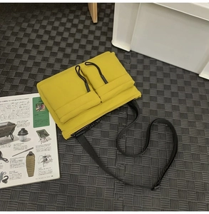 Detail of yellow nylon crossbody bag with dual flap pockets and black drawstrings