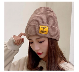 Detail of ribbed knit beanie in oatmeal with a yellow rectangular woven patch