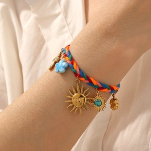 Colorful woven bracelet with golden sun and turquoise charms worn on a model's wrist