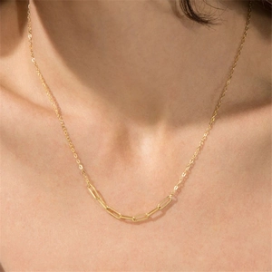 Detail of a golden paperclip link chain necklace worn on a woman's neck near the collarbone