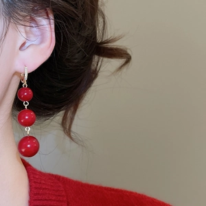 Close-up of elegant red resin triple bead drop earrings with gold diamond-encrusted clasps
