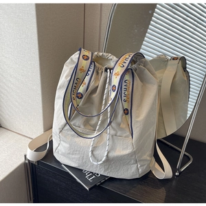 Detalle del bolso saco de nailon gris claro con correa tejida en colores azul y amarillo