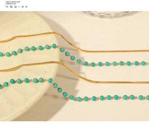 Detail of layered gold snake chain and turquoise bead necklace on ceramic plate