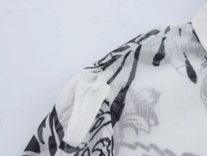 Detail of ruffled shoulder seam and floral print on sheer white chiffon shirt