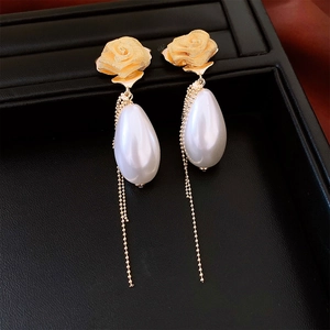 Detailed shot of gold rose earrings featuring pearl drops and delicate chain tassels