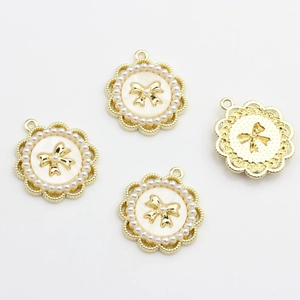 Detailed view of four golden alloy charms with white pearl edges and bow centers