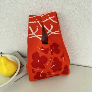 Detail of orange knitted tote bag featuring deep red floral patterns and white textures