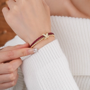 Detail of red braided leather bracelet with gold X-shaped cubic zirconia clasp on wrist