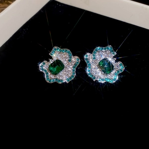 Macro shot of luxury emerald flower studs with silver diamonds on black velvet