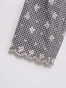 Détail du tissu vichy noir et blanc avec bords festonnés et broderies florales fines