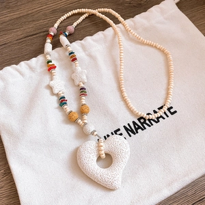 Detail of white porous heart pendant with woven beads on a rustic wooden surface