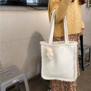 Detail of white leather tote bag featuring plush lamb wool trim and a cute bear charm