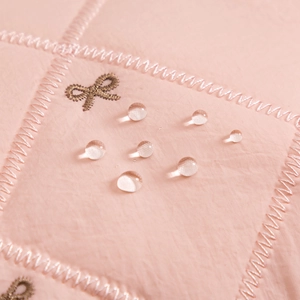 Close-up of pink quilted fabric showing water-resistant droplets and gold bow embroidery
