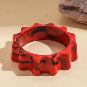 Dettaglio di un ampio bracciale in acrilico ondulato con texture marmorizzata rossa e nera