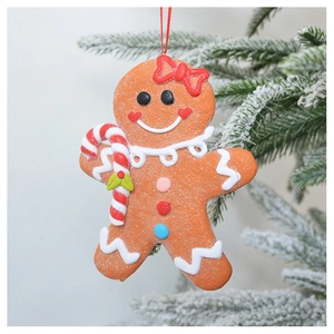 Close-up of glittery gingerbread man ornament hanging on a snowy Christmas tree branch
