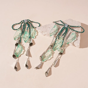 Sparkling green crystal bow tassel earrings with silver petals on a stone pedestal