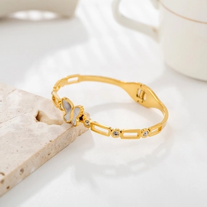 Detail of 18K gold butterfly bangle with shell inlay and crystals on stone background