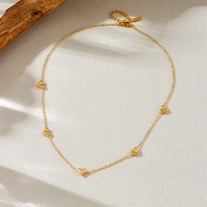 Gold stainless steel necklace with five sparkling heart pendants on a grey texture