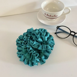 Detail of green satin scrunchie with pleated texture next to a white teacup and glasses