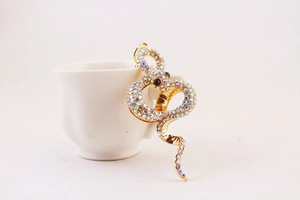 Detail of a gold snake keychain with iridescent rhinestones hanging on a white ceramic cup