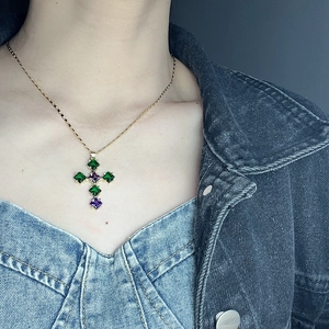 Detailed view of a gold cross necklace with vibrant green and purple cubic zirconia stones