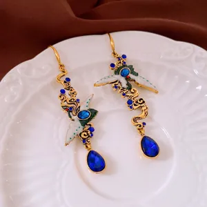 Elegant gold crane earrings with blue gems and enamel details on a white ceramic plate