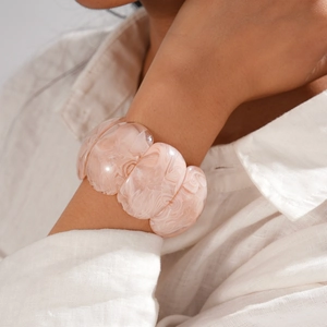 Détail d'un bracelet extensible en acrylique rose marbré sur un mannequin en lin blanc