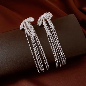Detailed close-up of silver bow tassel earrings with sparkling rhinestones on velvet stand