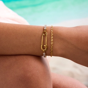 Close-up of double-layer gold paperclip chain bracelet with zircon-set safety pin charm
