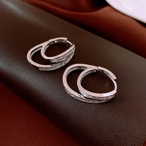 Close-up of double-layered silver hoop earrings with cubic zirconia on brown leather