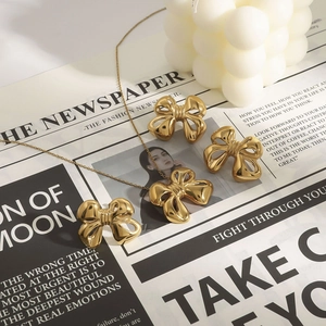 Elegant gold bow necklace and earrings set displayed on a vintage newspaper background