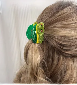 Detail view of a cute green frog hair claw clip styled on a model with blonde wavy hair