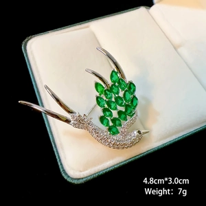 Detailed size view of silver swallow brooch with green gemstones on white velvet