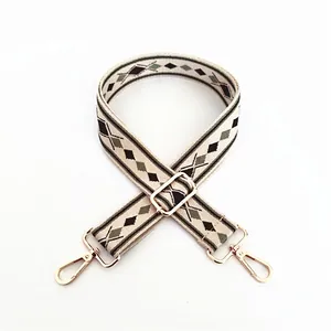 Detailed view of beige bag strap with green geometric patterns and gold metal hooks