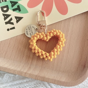 Detail of yellow handmade beaded heart keychain with engraved alloy tag on wooden tray