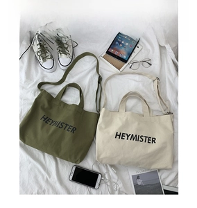 Detailed view of olive green and beige canvas bags with HEYMISTER print and dual straps