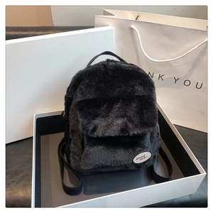 Mochila de peluche negra con parche presentada en una caja de regalo elegante