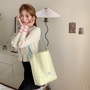 Detail of light yellow quilted tote bag featuring heart pattern embroidery and blue strap