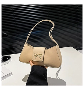 Detail of beige faux leather baguette bag featuring a gold bow accent and sleek shoulder strap