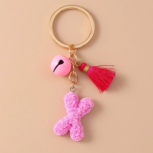 Detailed close-up of pink rose letter X keychain with bell and stylish tassel pendant