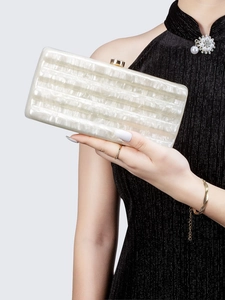 Close-up of white acrylic evening clutch bag with striped texture and gold clasp