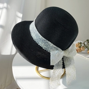 Elegant black straw sun hat with white lace bow decoration on a white table