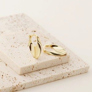 Polished golden U-shaped earrings displayed on a beige stone base for luxury look